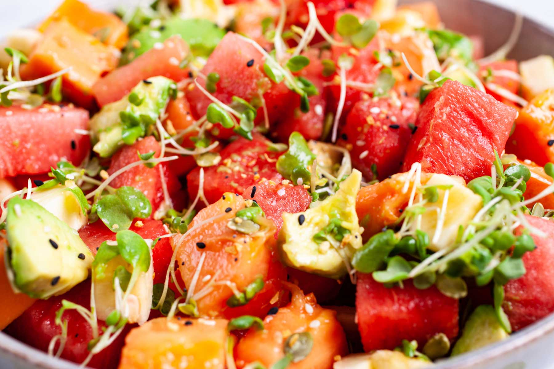 A watermelon fruit salad with papaya and avocado and crunchy seeds served in a bowl.