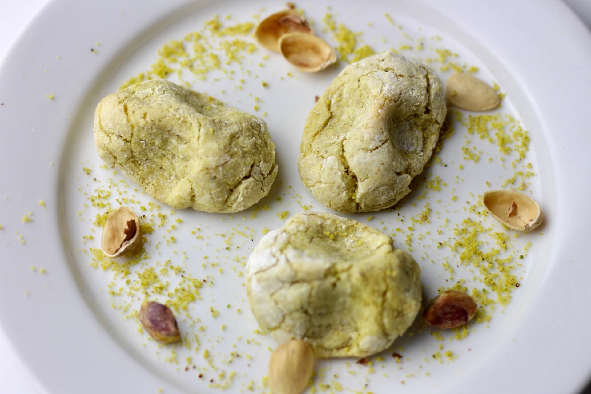 Drie pistachekoekjes geserveerd op een bord met pistachenootjes als decoratie.