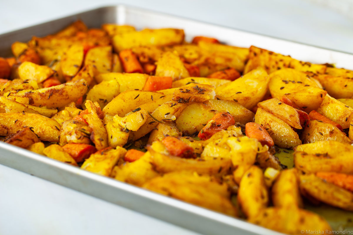 Oven-baked Potatoes with Jamaican Curry and Caraway Fruits in oven tray