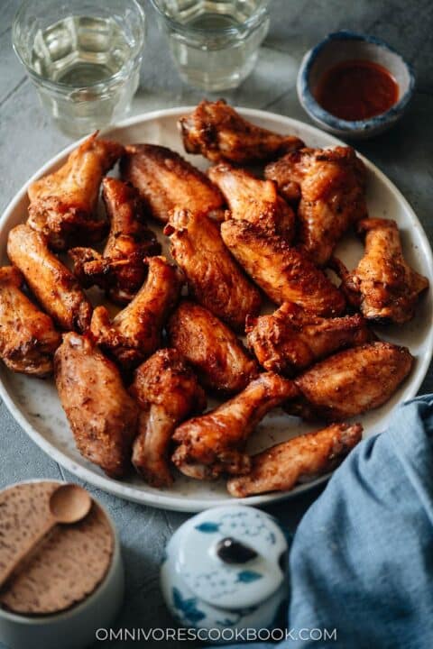a white plate full of baked sichuan chicken wings with water glasses in the back ground.