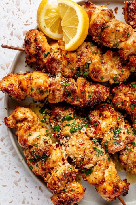 an up close shot of garlic parmesan chicken skewers with slices of lemon on the side of the plate.