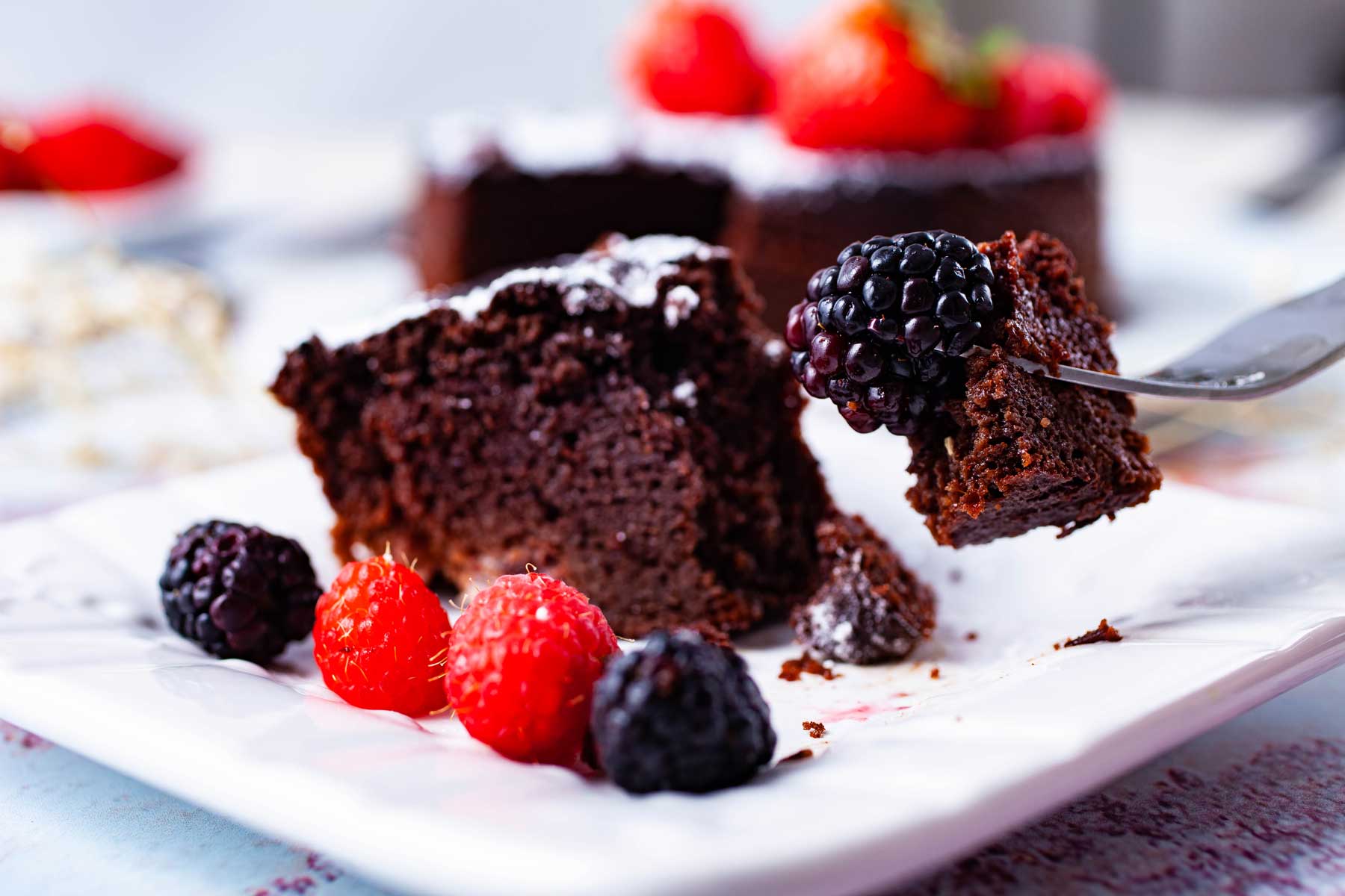 A fork holding up a bite out of a berry topped rich chocolate cake.