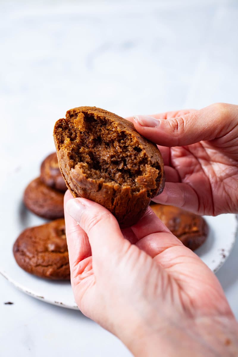 A hand breaking a soft baked flourless peanut butter cookie in half.