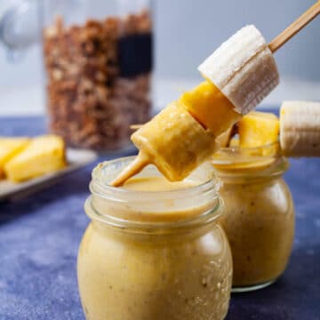 A hand dipping a fruit stick into a smoothie.