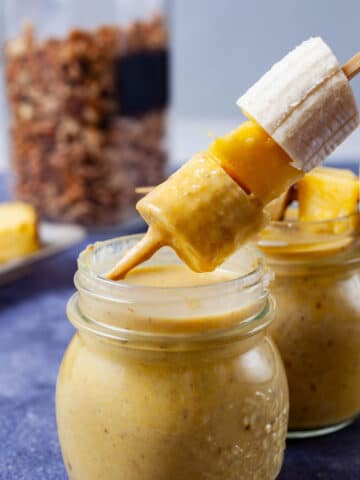 A hand dipping a fruit stick into a smoothie.