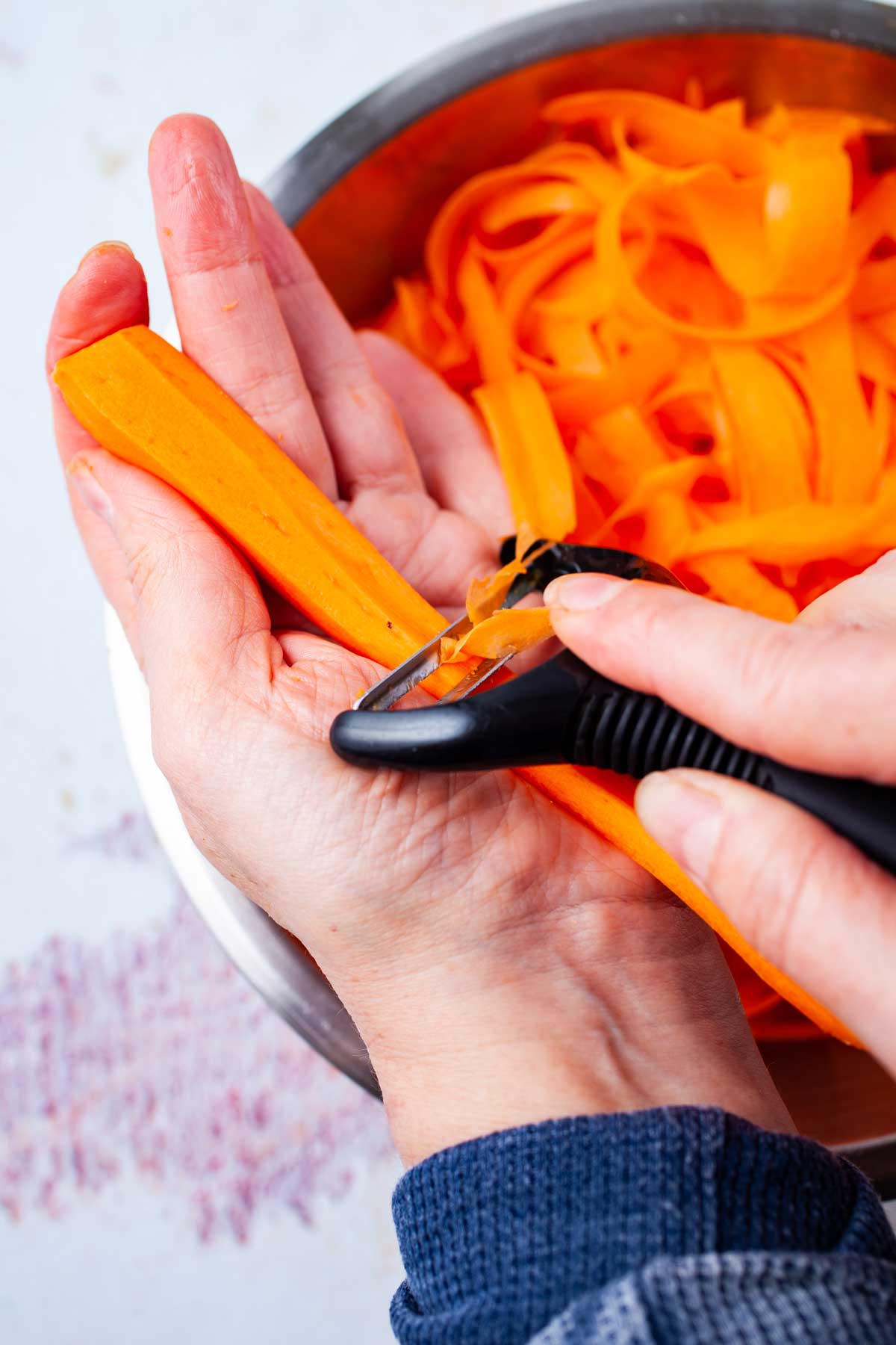 A hand shaving off carrot slices with a peeler.