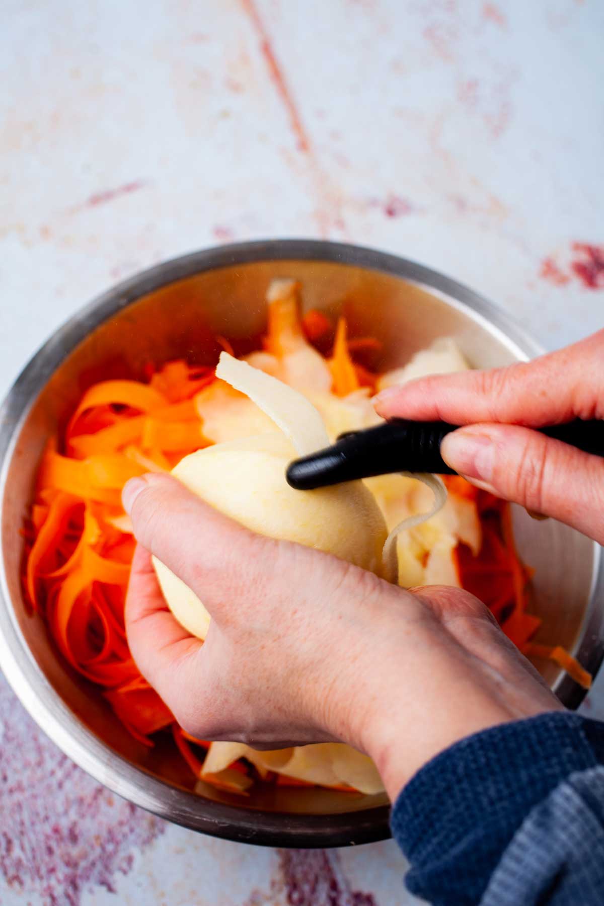 A hand shaving off apple slices with a peeler.