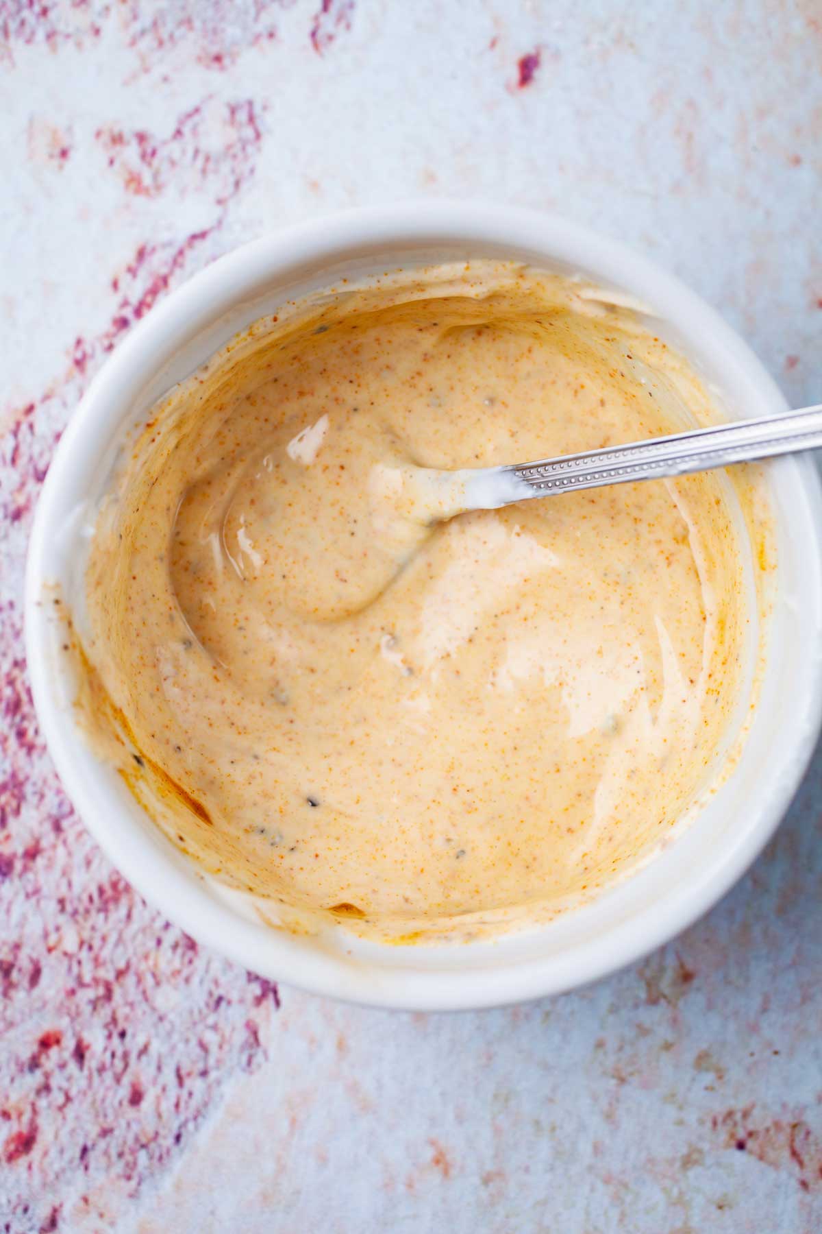 A teaspoon resting in a creamy salad dressing.