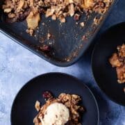 Healthy apple crumble served on a plate and topped with a scoop of ice cream next to a baking dish with the same apple crumble.