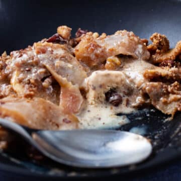 A close-up of a spoon resting in a plate with ice cream melted in a baked apple crisp.