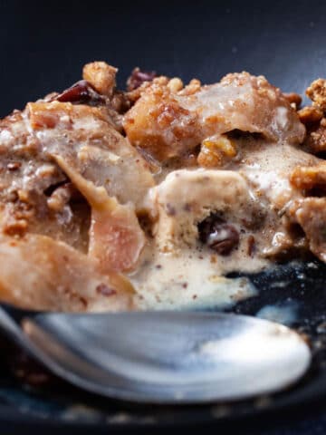 A close-up of a spoon resting in a plate with ice cream melted in a baked apple crisp.