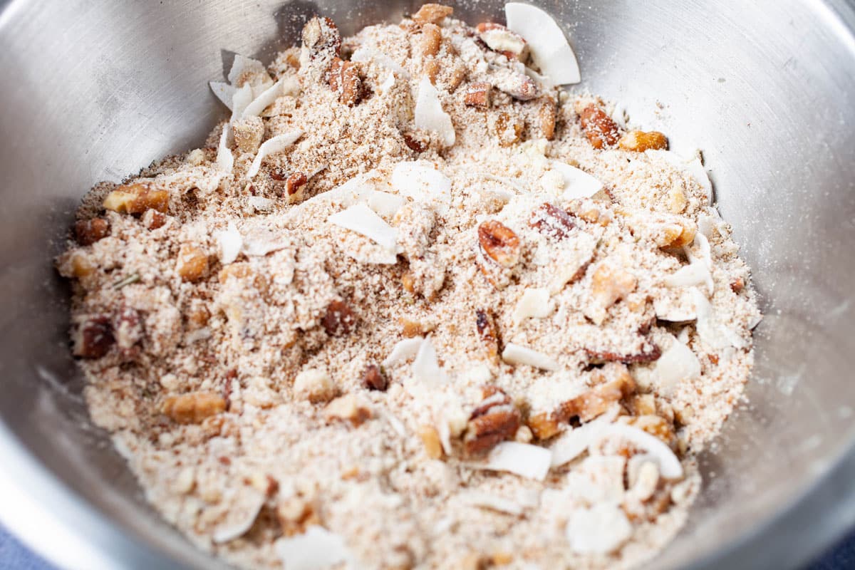 A dry flour mix with nuts and coconut shreds in a stainless steel bowl.
