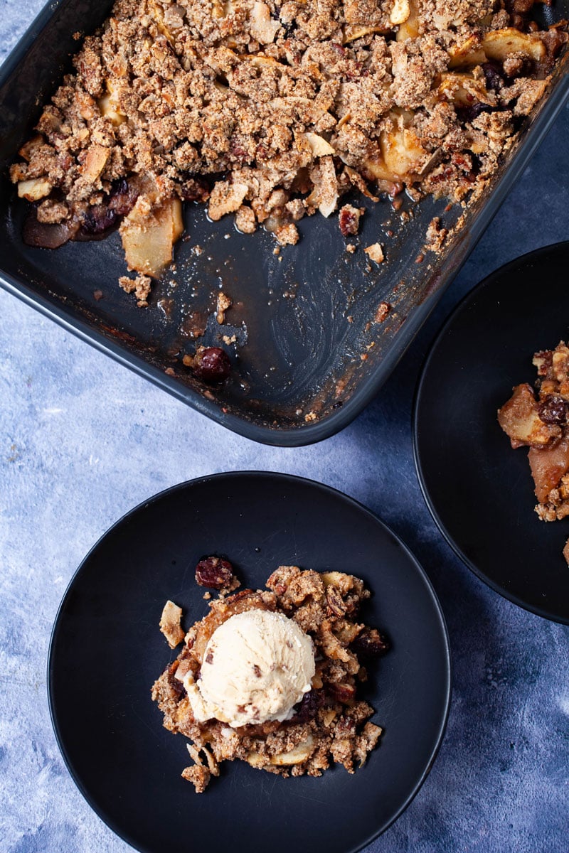 Healthy no oats apple crisp served in a plate and topped with a scoop of ice cream next to half full baking dish with the same apple crisp.