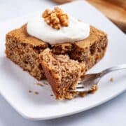 A piece of gluten-free applesauce cake with walnuts topped with yogurt.