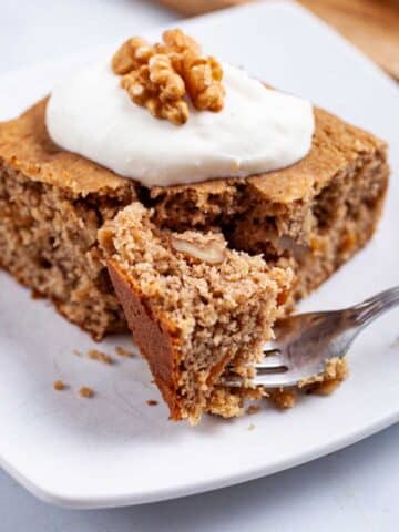 A piece of gluten-free applesauce cake with walnuts topped with yogurt.