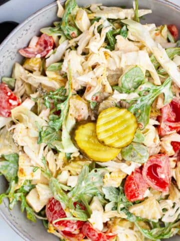 Creamy arugula and cabbage salad with sweet mini tomatoes and pickles served on a plate.