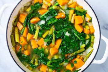 Sweet potatoes, spinach, onions, chopped asparagus, and broth in a large Dutch pan.