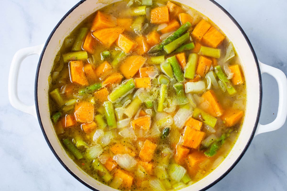 Chopped sweet potatoes, asparagus, onions, and broth in a large Dutch pan.