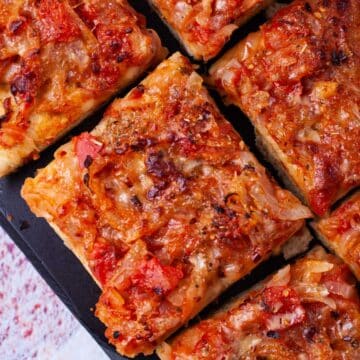 Thick-crust Sicilian pizza with onion-based toppings on a cutting board.