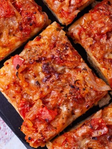 Thick-crust Sicilian pizza with onion-based toppings on a cutting board.
