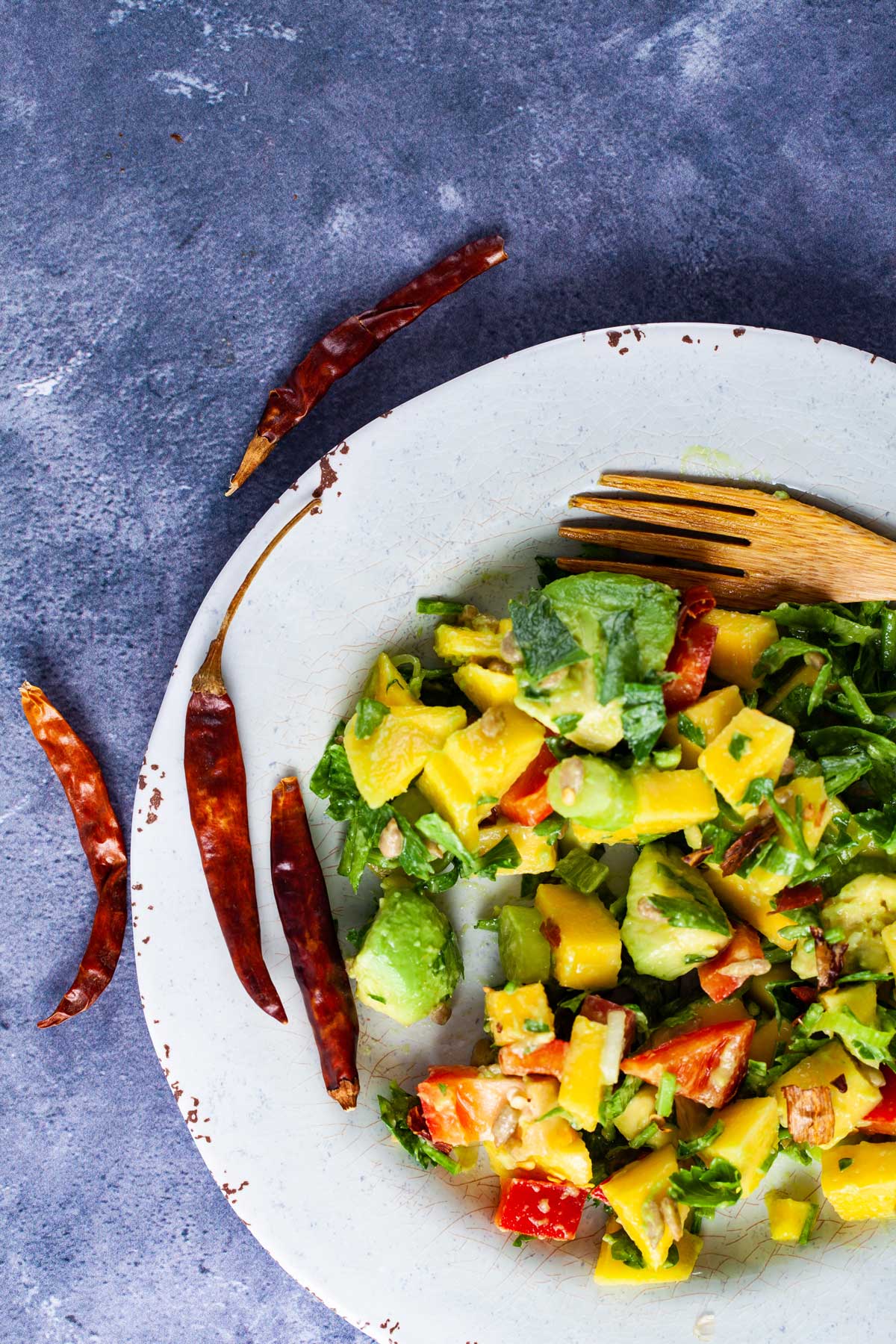 Mango avocado salad displayed on a plate with a wooden fork and dried red peppers on the side.