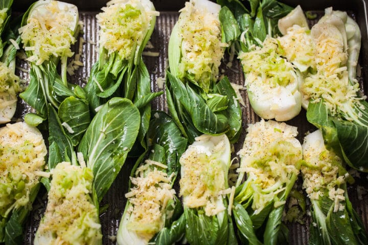 A large tray of lengthwise cut baby Bok Choy topped with grated cheese, grated apples, and black pepper grinds.