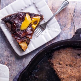 A pie-like piece of a large apple bacon pancake cut out and served on a small plate with a fork on the side.