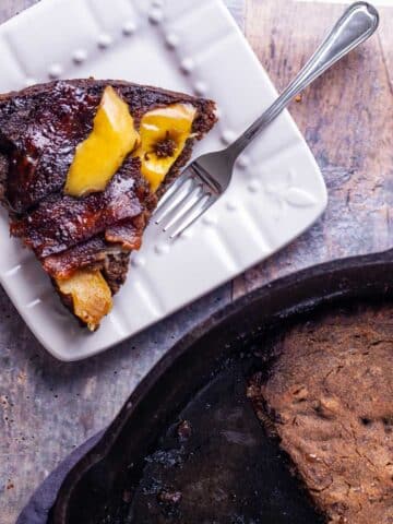 A pie-like piece of a large apple bacon pancake cut out and served on a small plate with a fork on the side.