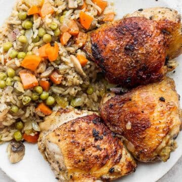 Three bone-in baked chicken thighs served with rice and veggies on a plate.
