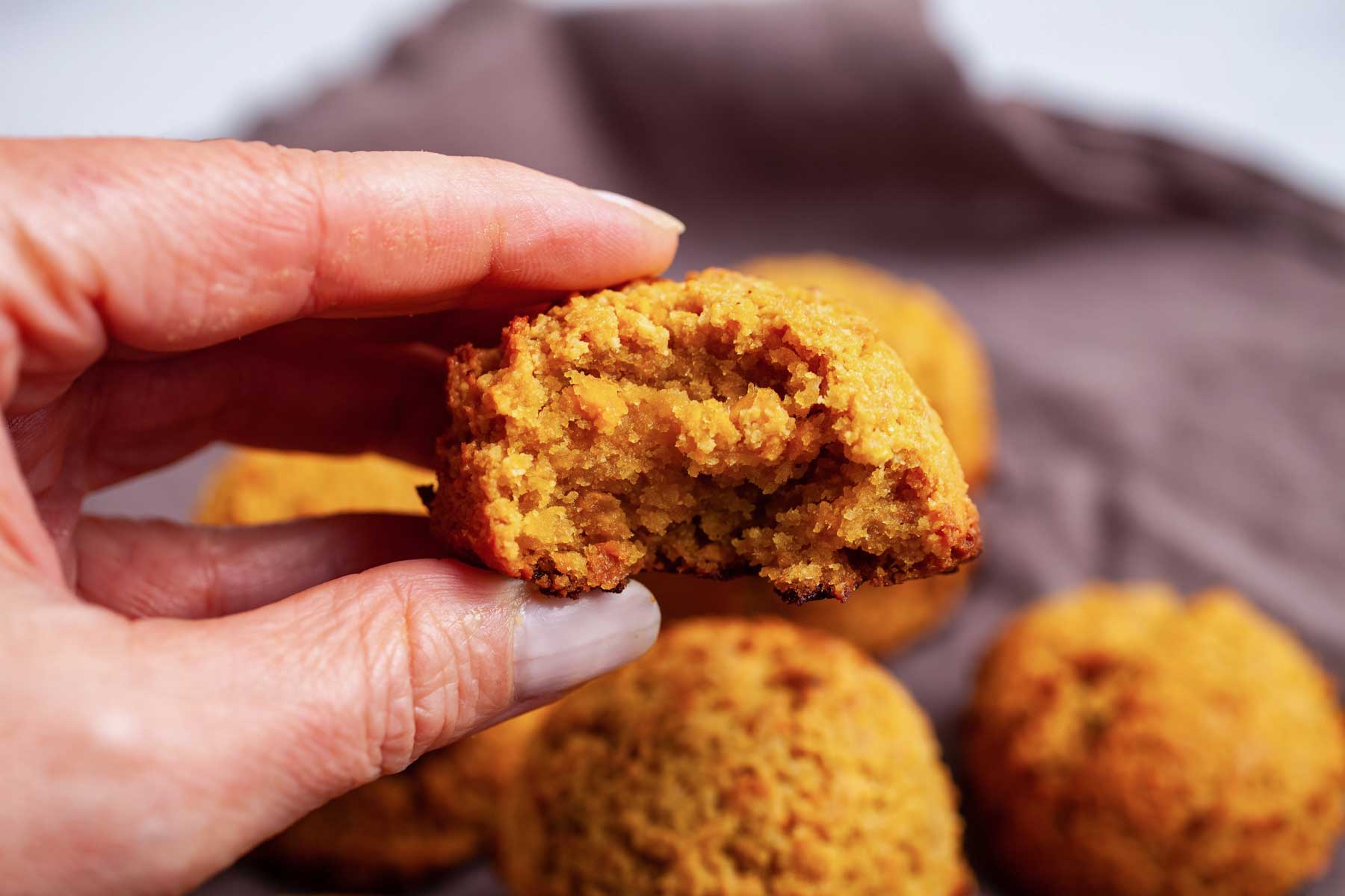 A hand holding a mango cookie with a bite taken out of it.