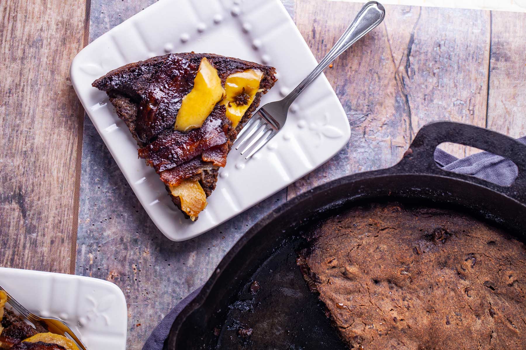 A pie-like piece of a large apple bacon pancake cut out and served on a small plate with a fork on the side.