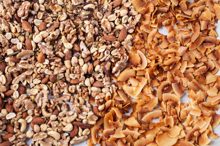 A mix of roasted nuts and coconut shreds spread out on a prepared baking sheet.