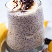 A cup full of banana chia pudding topped with fresh banana slices and shaved chocolate.