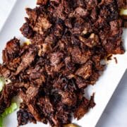 A large serving plate with shredded beef tacos chuck roast.