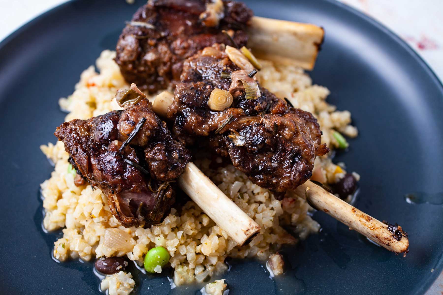 A plate containing cauliflower rice and topped with fall of the bone beef ribs.