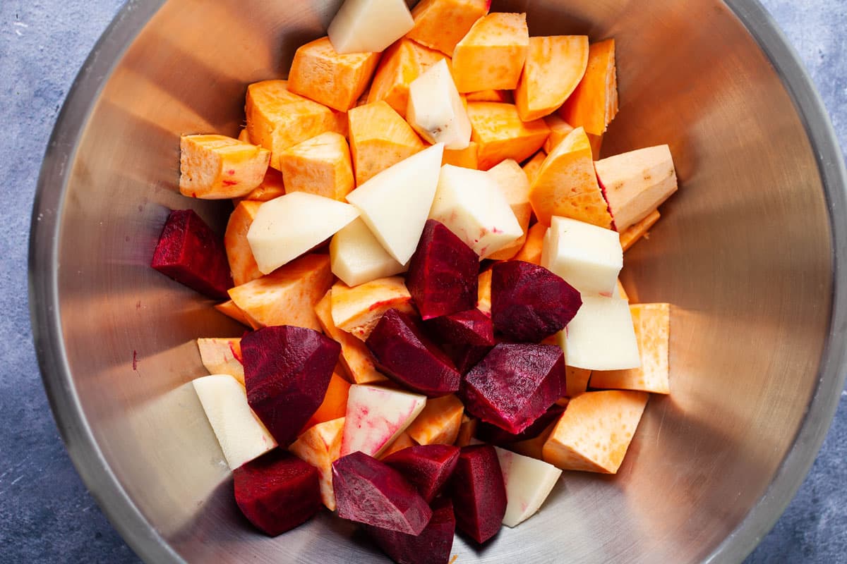 A stainless steel bowl filled with peeled and chopped potatoes and beets.