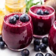 Beetroot and blueberry smoothie shots on a table and garnished with extra blueberries.