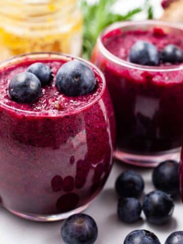 Beetroot and blueberry smoothie shots on a table and garnished with extra blueberries.