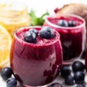 Beetroot and blueberry smoothie shots on a table and garnished with extra blueberries.