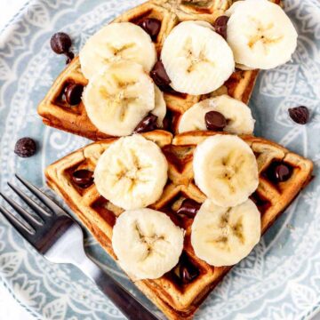 Two mini waffles on a plate topped with banana and melted chocolate.