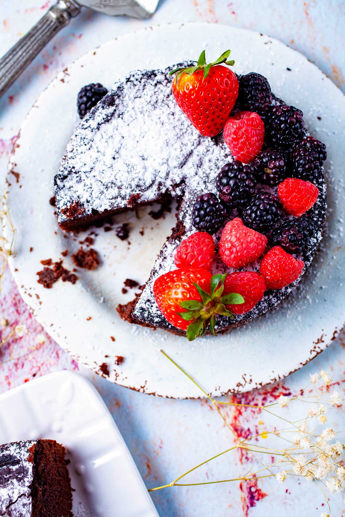 A piece taken out of a mini flourless chocolate cake served with fresh berries and topped with powdered sugar.