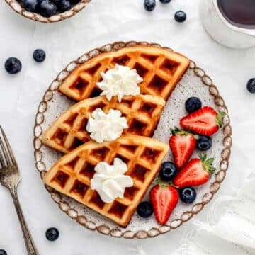 Three mini waffles on a plate topped with whip cream.