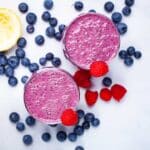Two purple blueberry and raspberry smoothies on a table.