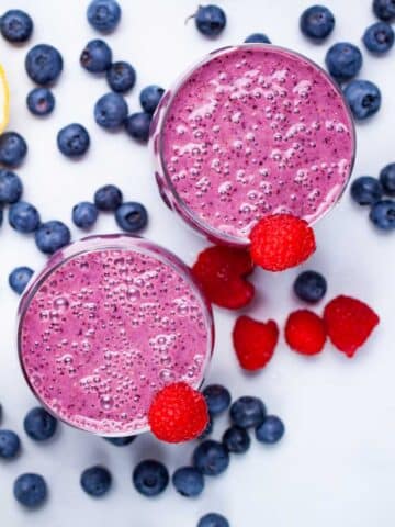 Two purple blueberry and raspberry smoothies on a table.