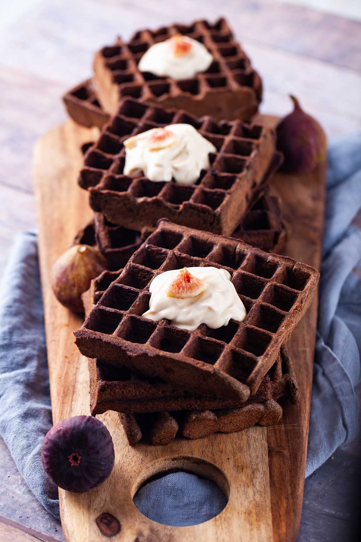 Buckwheat waffles topped with a dollop of yogurt and fresh figs served on a wooden board.