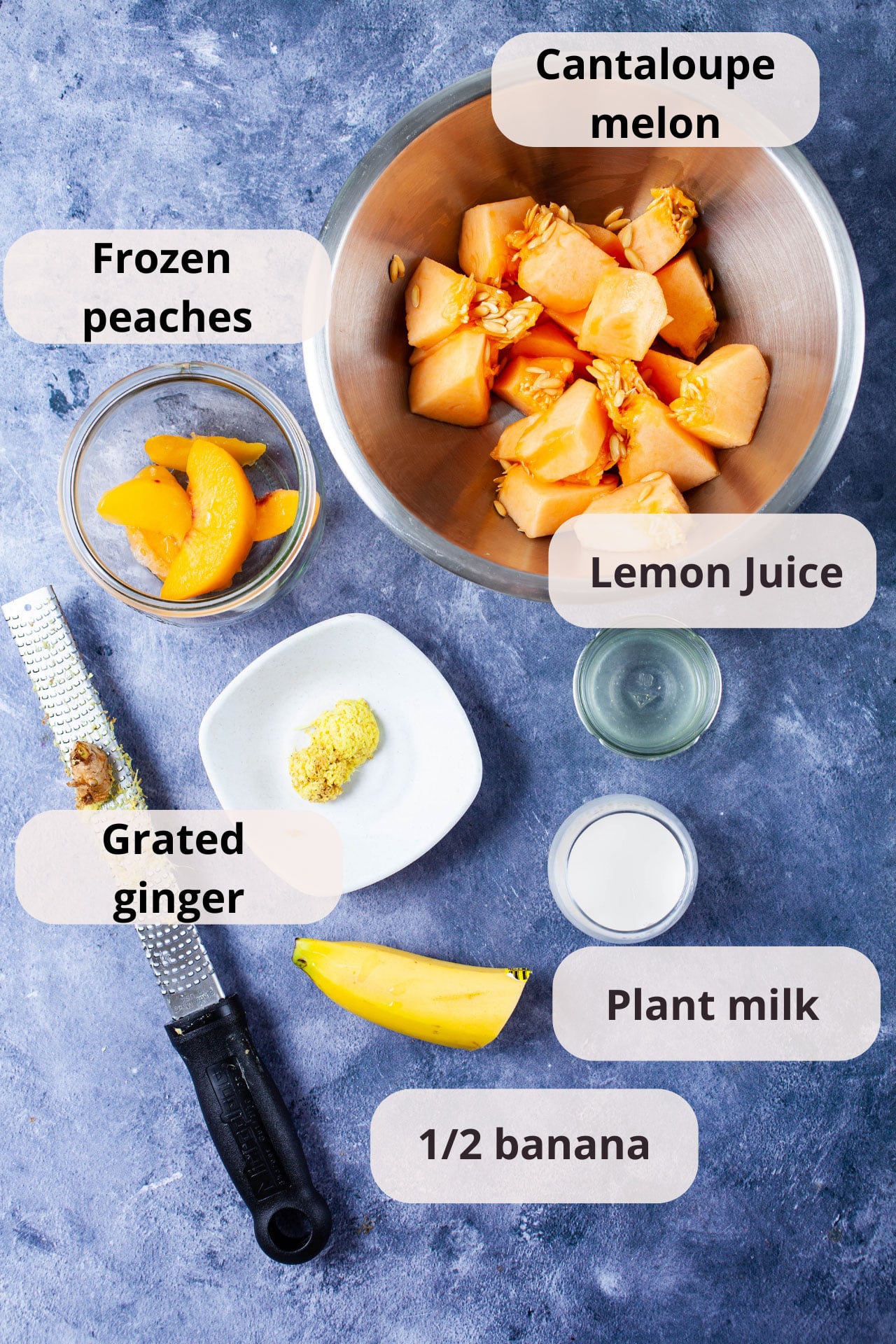 Cantaloupe melon, frozen peaches, lemon juice, grated ginger, plant milk, and half a banana displayed on a table.