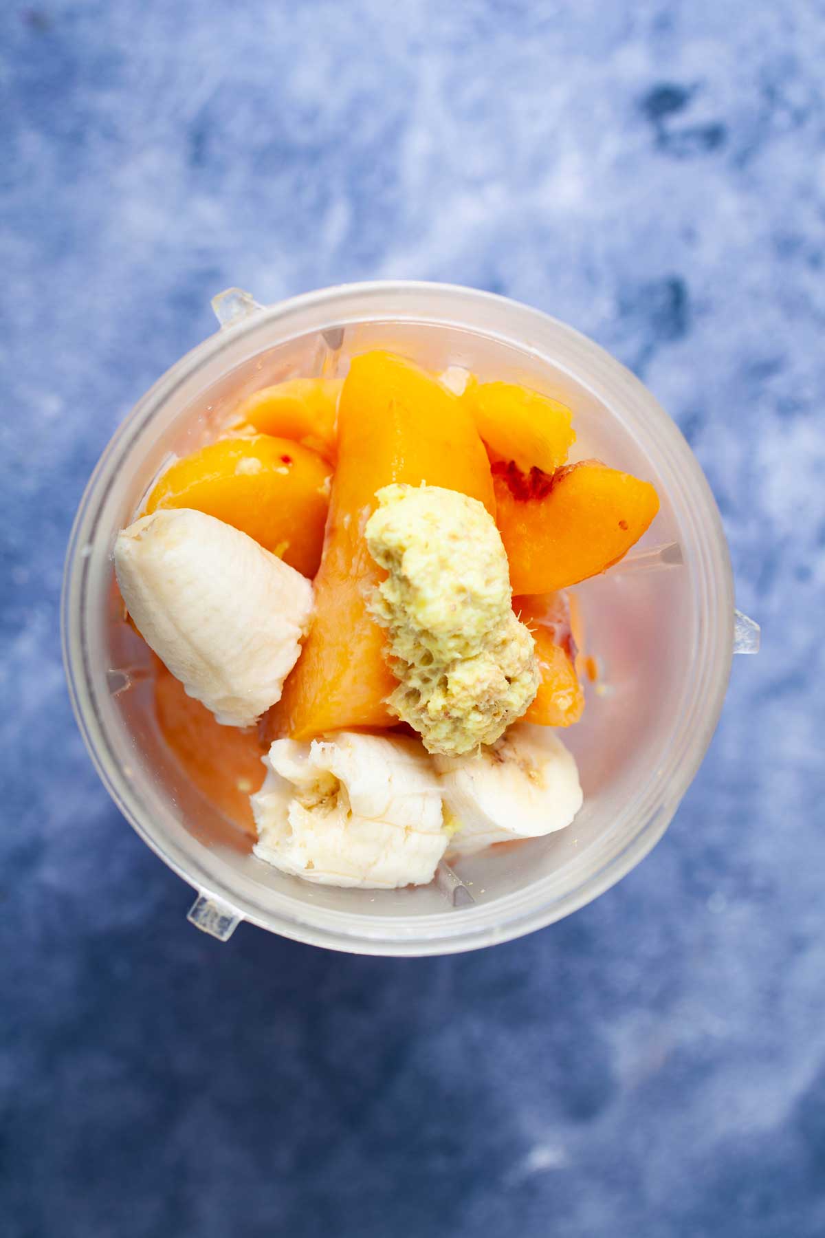 A blender cup with cantaloupe pieces, frozen peaches, pieces of banana, and grated ginger.