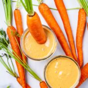 Two carrot and banana smoothies on a table and served with raw carrots.