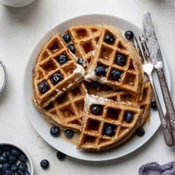 Waffles on a plate topped with blueberries and syrup.