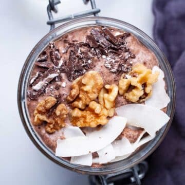 A chocolate chia pudding in a mason jar topped with coconut flakes, walnuts, and dark chocolate bits.